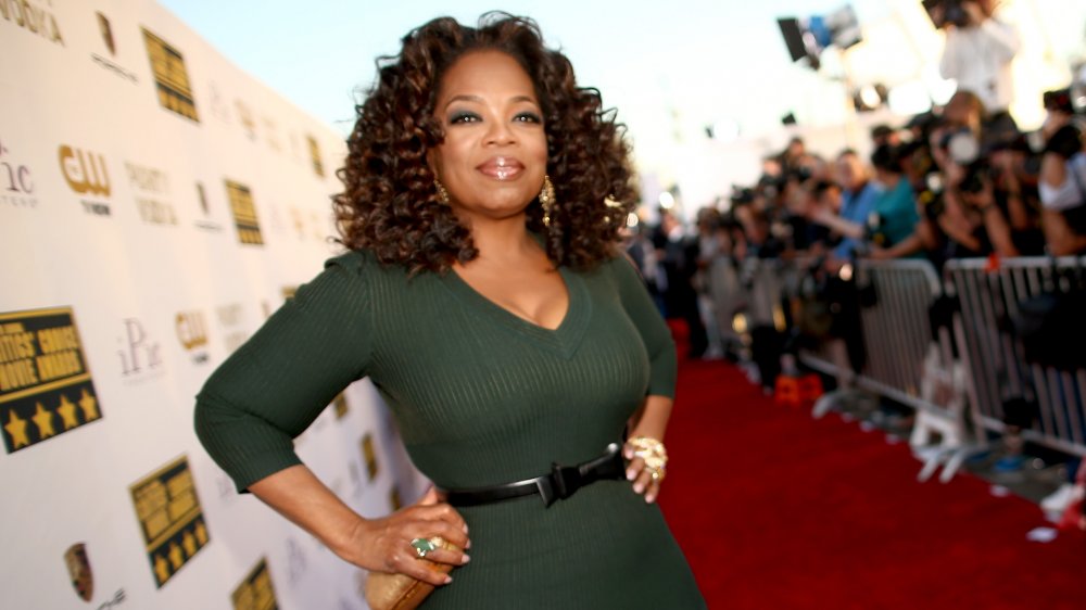 Oprah Winfrey with a small smile and hands on her hips on the red carpet of the Critics' Choice Movie Awards