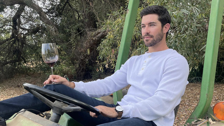 Spencer Robertson holding a wine glass on a tractor