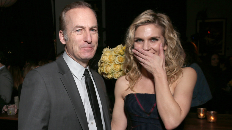 Bob Odenkirk smiles at the camera as Rhea Seehorn covers her mouth excitedly