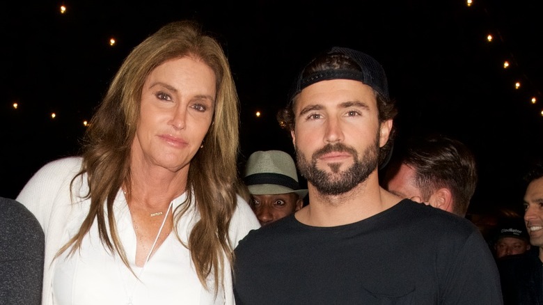 Caitlyn Jenner, not smiling, wearing white blouse, with arm around Brody Jenner, not smiling, wearing black, wearing a hat, 20216 photo