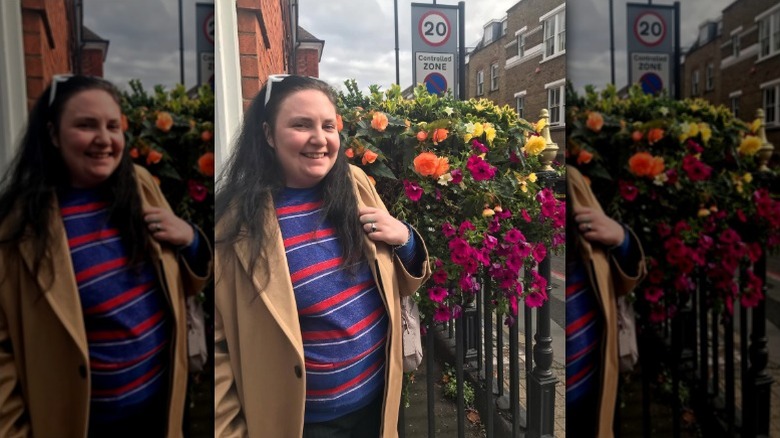 Lena Dunham smiles in front of flowers in London