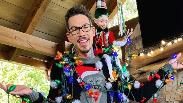 David Bromstad wrapped in Christmas lights with toy elf on shoulder