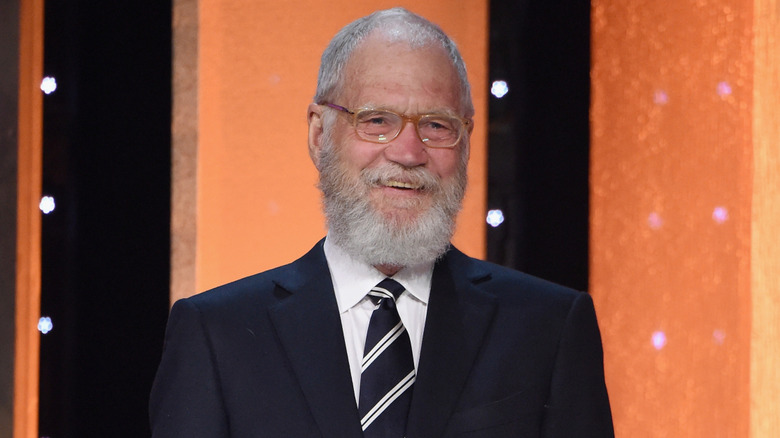 David Letterman onstage smiling in suit and glasses with a white beard