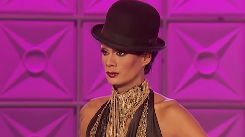Raja on the runway in gold chains and a hat
