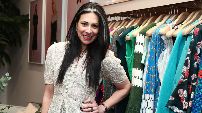 Stacy London grinning next to rack of clothes