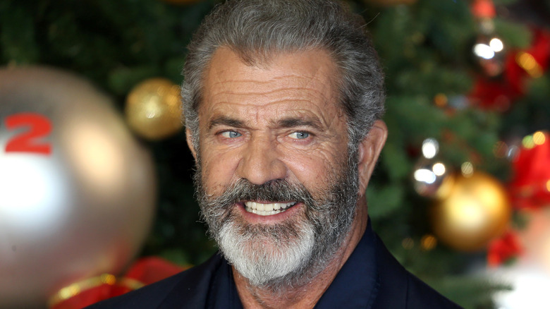 Mel Gibson grinning by a Christmas tree