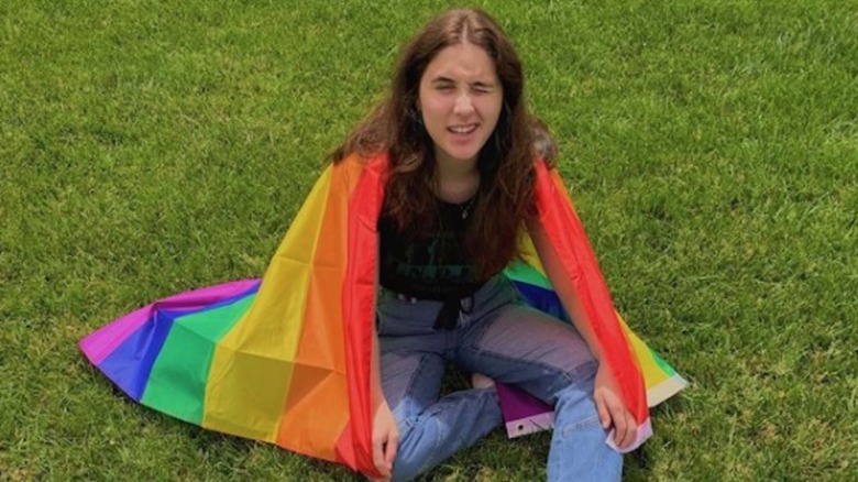 Max Dubrow sitting on the grass, draped in a rainbow flag 