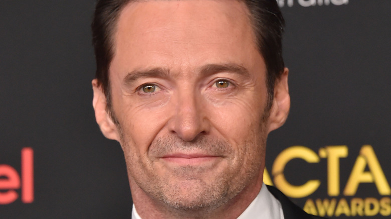 Hugh Jackman grins slightly on red carpet