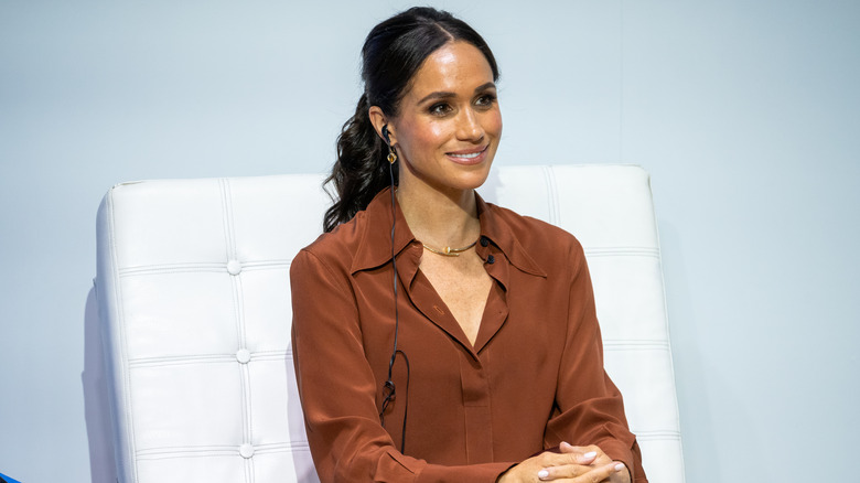 Meghan Markle wearing brown on a white chair