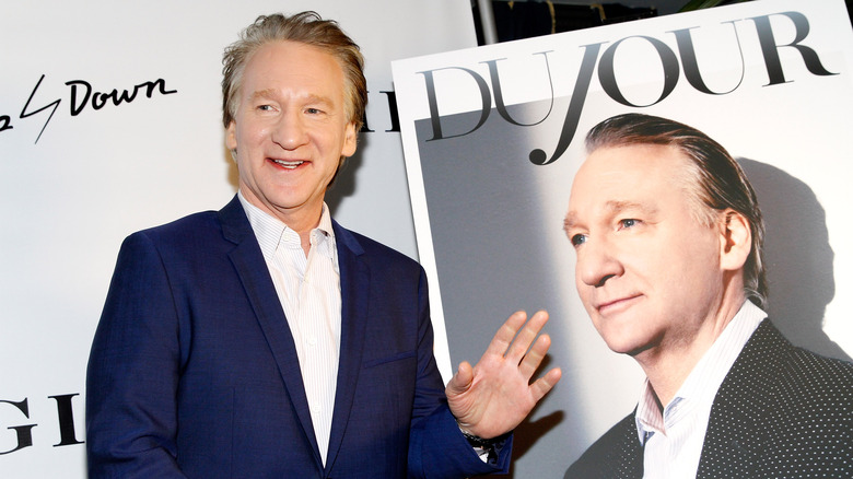 Bill Maher posing in front of a poster of himself 