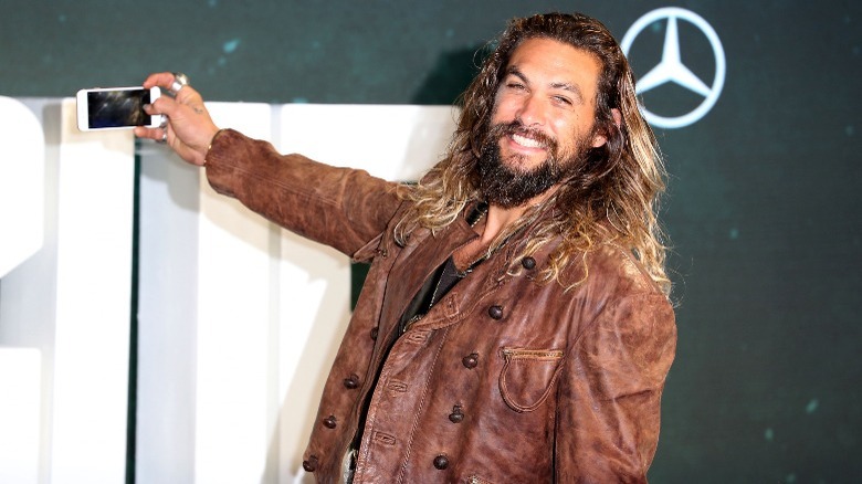 Jason Momoa smiling while taking photo with iphone