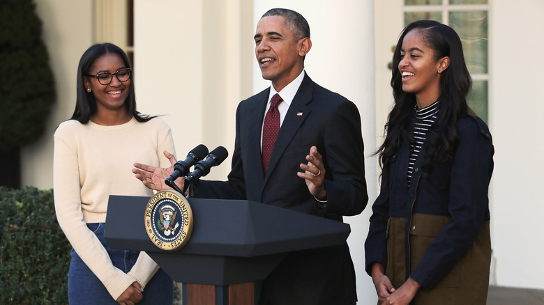 Sasha, Barack, and Malia Obama laughing at podium