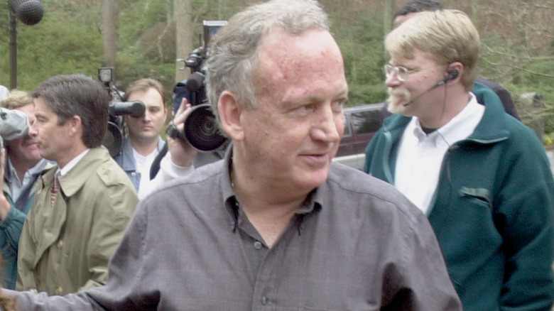 John Ramsey wearing a gray shirt surrounded by cameras