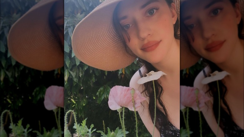 Kat Dennings posing in a sun hat in her garden with poppy flowers