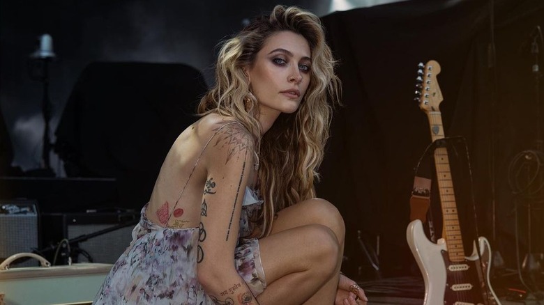 Paris Jackson wearing a strappy floral dress posing next to a guitar