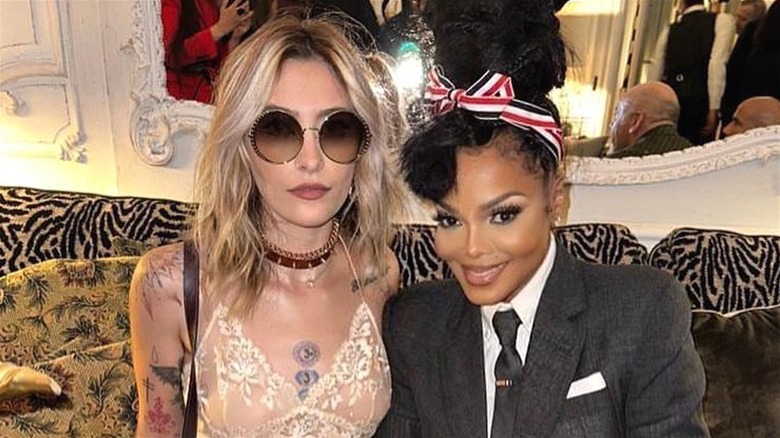 Paris Jackson wearing a lace tank top and sunglasses with Janet Jackson wearing a black jacket, white shirt, and black tie