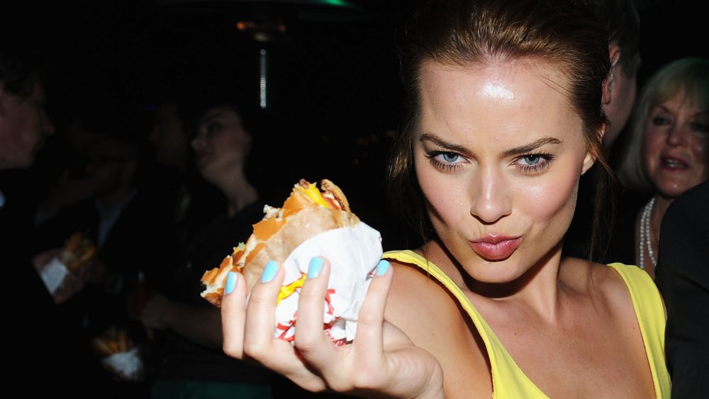 Margot Robbie holding a burger, making a funny face