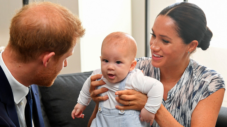 Prince Harry sitting with Meghan Markle holding Archie