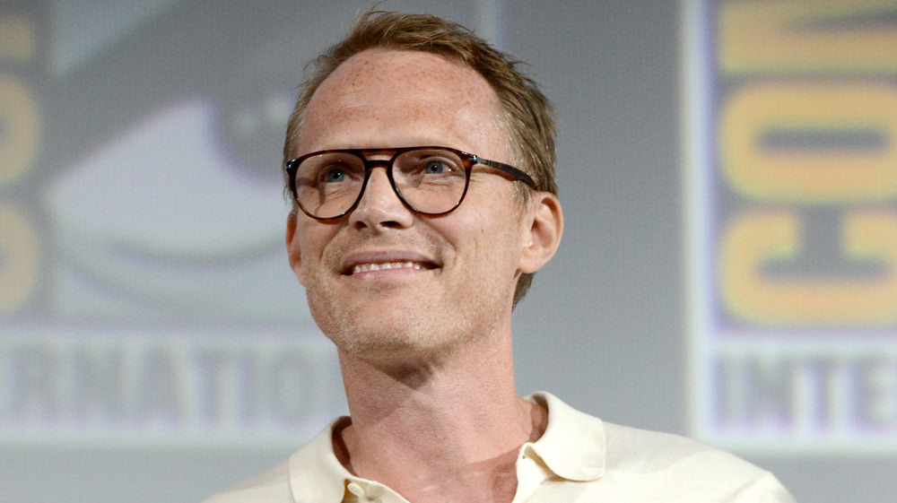 Paul Bettany looks to his right smiling wearing a pair of thickly rimmed glasses