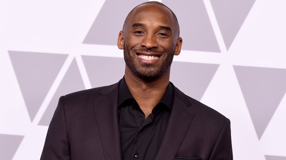 Kobe Bryant in an all-black suit, smiling