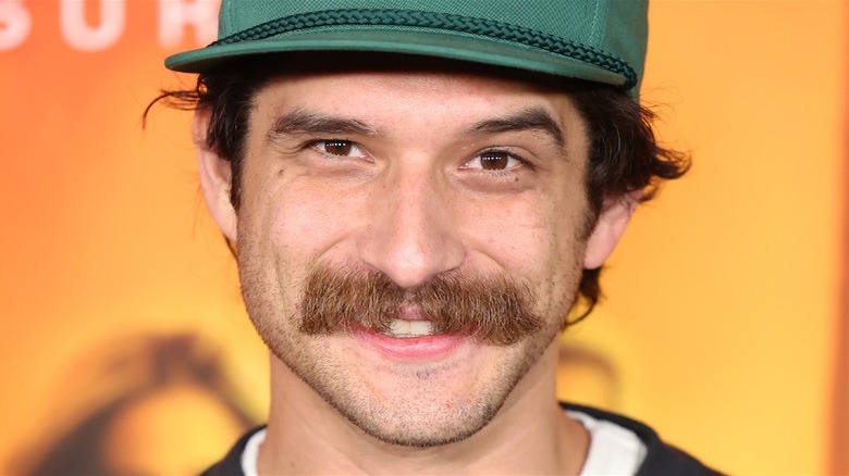 Tyler Posey smiling, orange background mustache