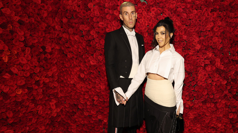 Travis and Kourtney pose in front of a wall of roses