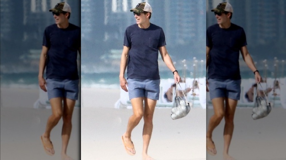 Jared Kushner on the beach smiling, wearing a bathing suit and sandals 