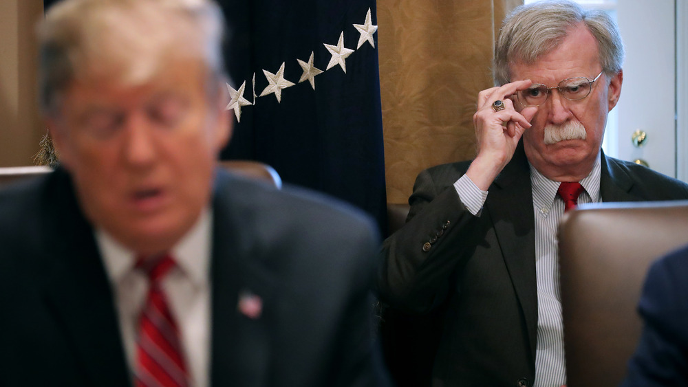 Former national security advisor John Bolton looking at an out of focus former President Trump in the foreground 