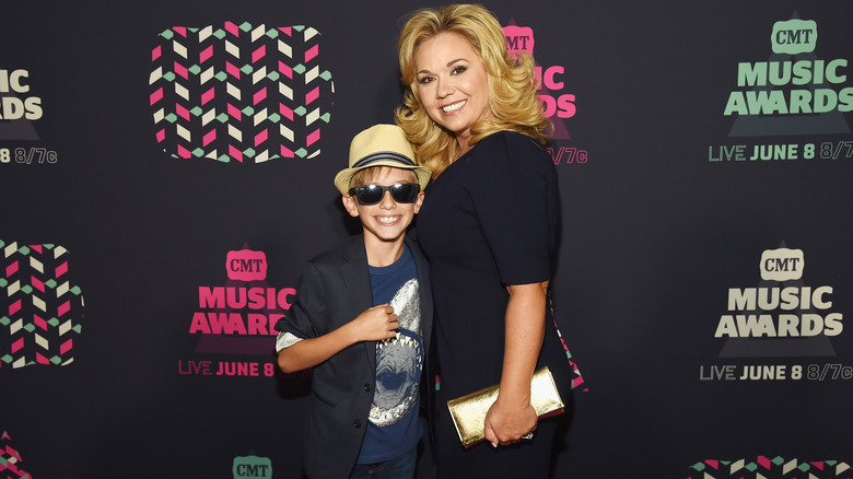 A young Grayson Chrisley, on a red carpet wearing sunglasses, with mom Julie Chrisley 