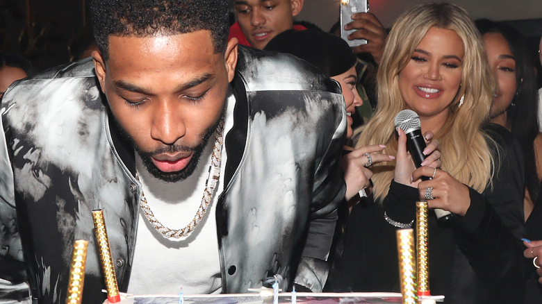 Tristan Thompson blowing out candles with smiling Khloe Kardashian