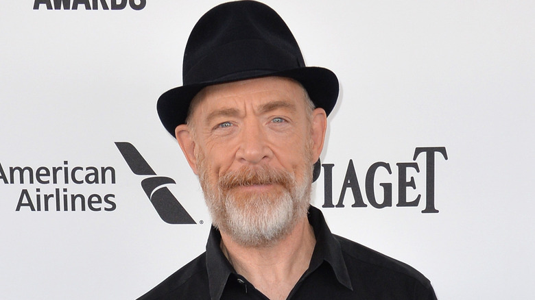 J. K. Simmons smiling in black hat