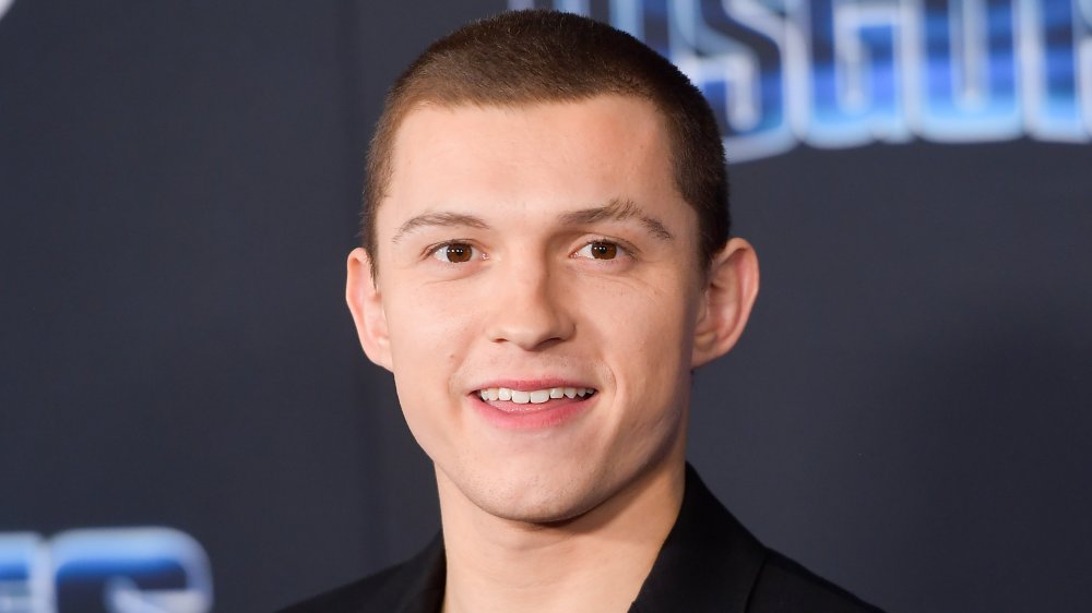 Tom Holland with a buzz cut, smiling at a movie premiere