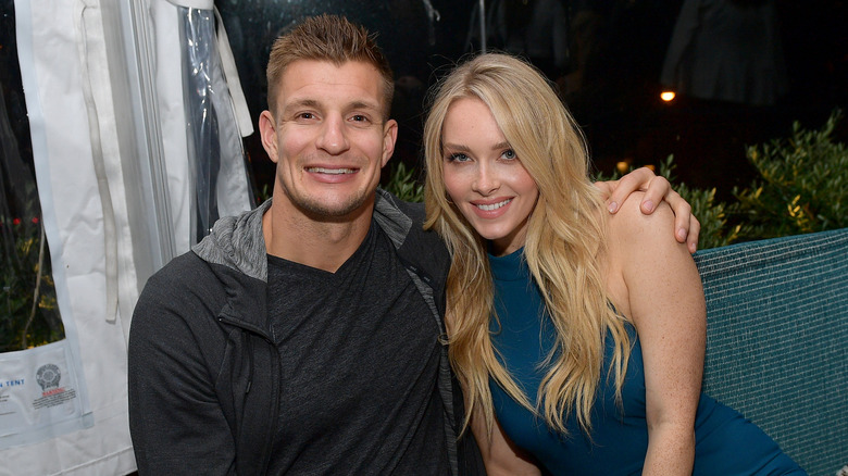 Rob Gronkowski wearing a grey jacket and grey t-shirt with Camille Kostek wearing a teal high neck sleeveless dress