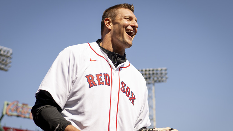 Rob Gronkowski smiling while wearing a white Boston Red Sox baseball jersey and black long sleeved shirt