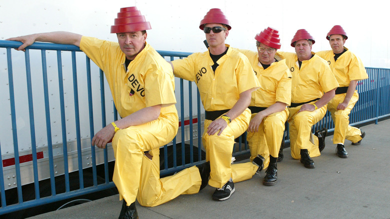 Devo band members all kneeling together in yellow jumpsuits and red tiered hats