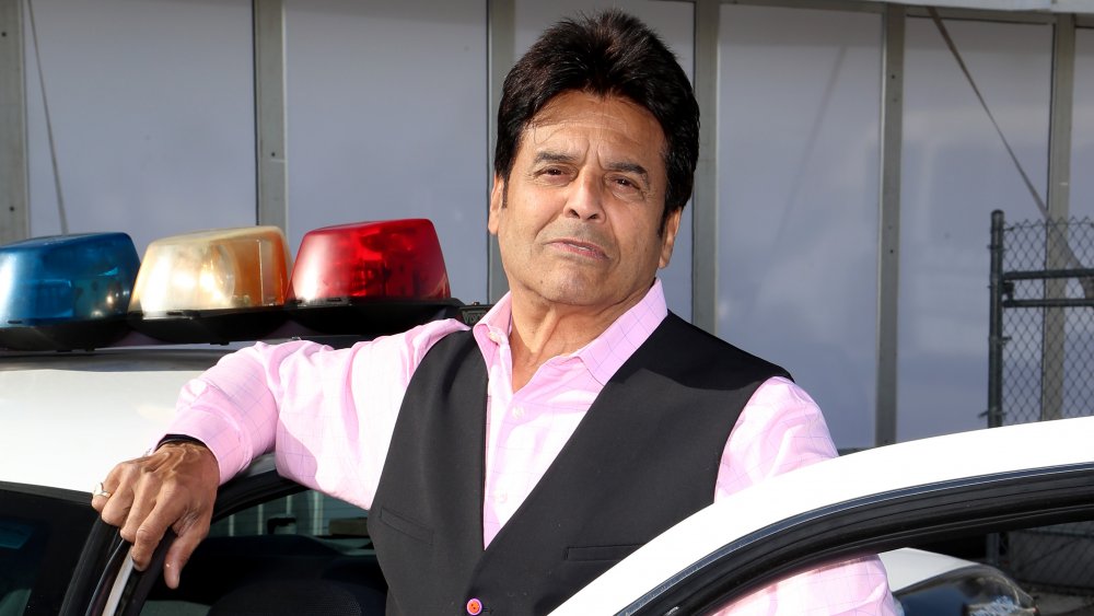 Erik Estrada posing next to a police cruiser 