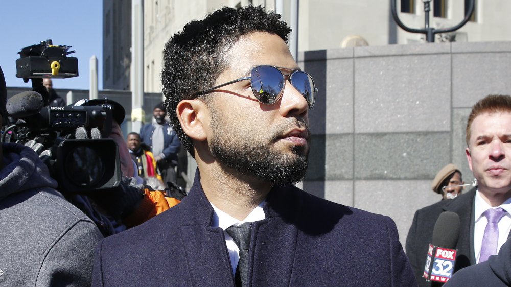 Jussie Smollett walking outside a courthouse, wearing sunglasses and surrounded by reporters