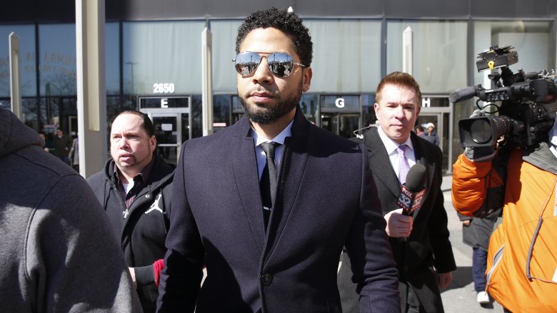 Jussie Smollett walking outside, wearing sunglasses, while surrounded by reporters