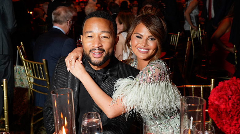 Chrissy Teigen and John Legend at dinner table hugging