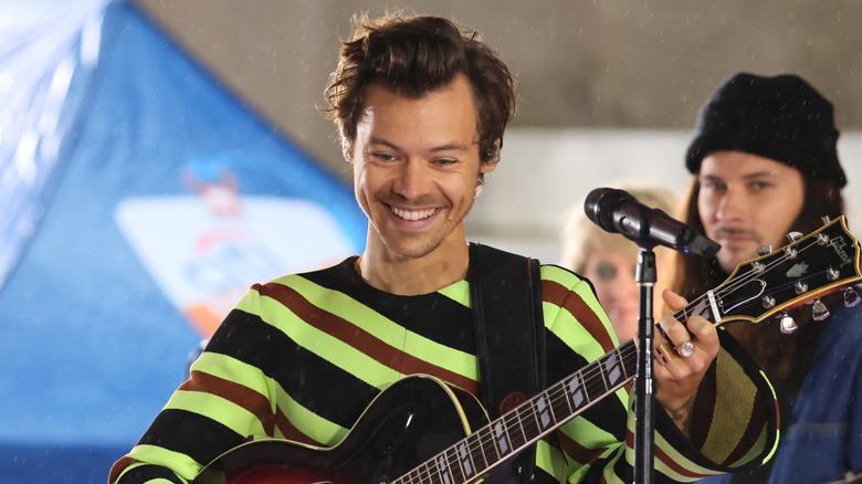 Harry Styles smiling as he plays guitar