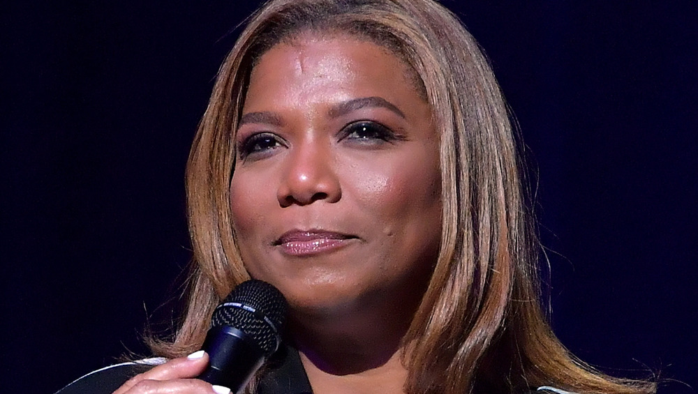 Queen Latifah speaking into a microphone while wearing a bomber jacket