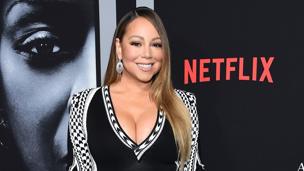 Mariah Carey in black in white dress, posing in front of Netflix wall