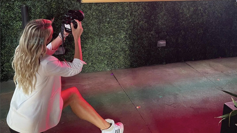 Olivia Flowers sit on the ground at an event, holding up a camera