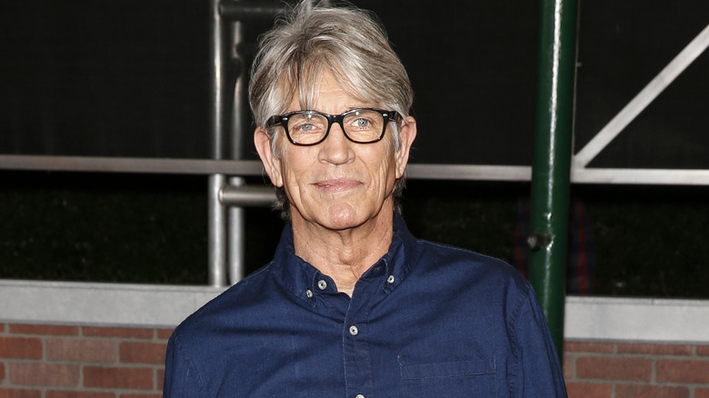 Eric Roberts poses in black-frame glasses and denim shirt