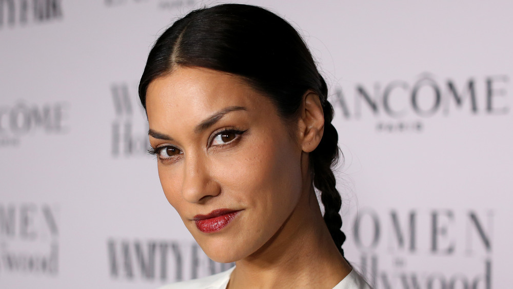 Janina Gavankar smiling sideways at the camera