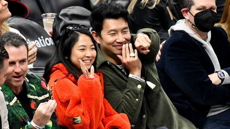 Allison Hsu and Simu Liu smile and wave at a sports match