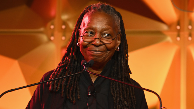 Whoopi Goldberg smirking at a podium