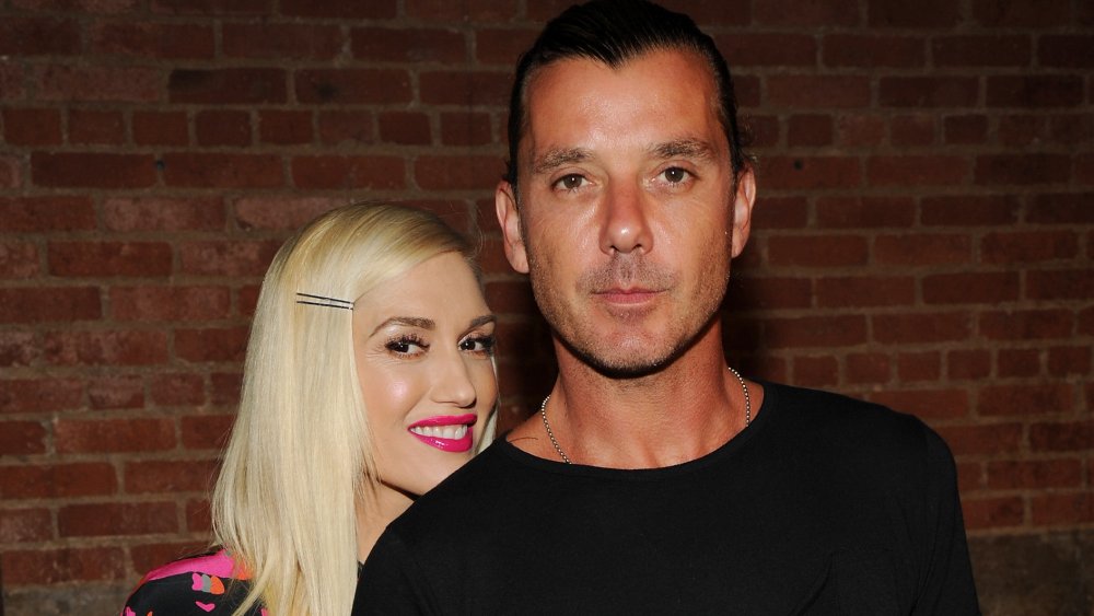 Gwen Stefani in a pink-and-black dress, smiling from behind Gavin Rossdale