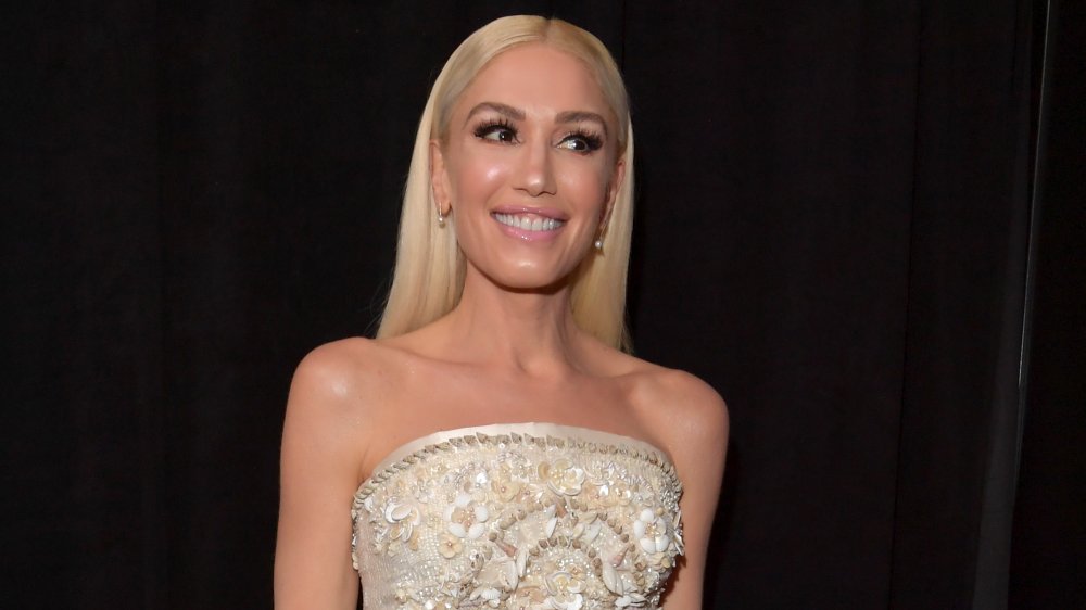 Gwen Stefani in a bejeweled white dress, smiling while looking off to the side