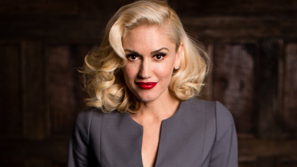 Gwen Stefani in a grey outfit and red lipstick, posing with a small smile